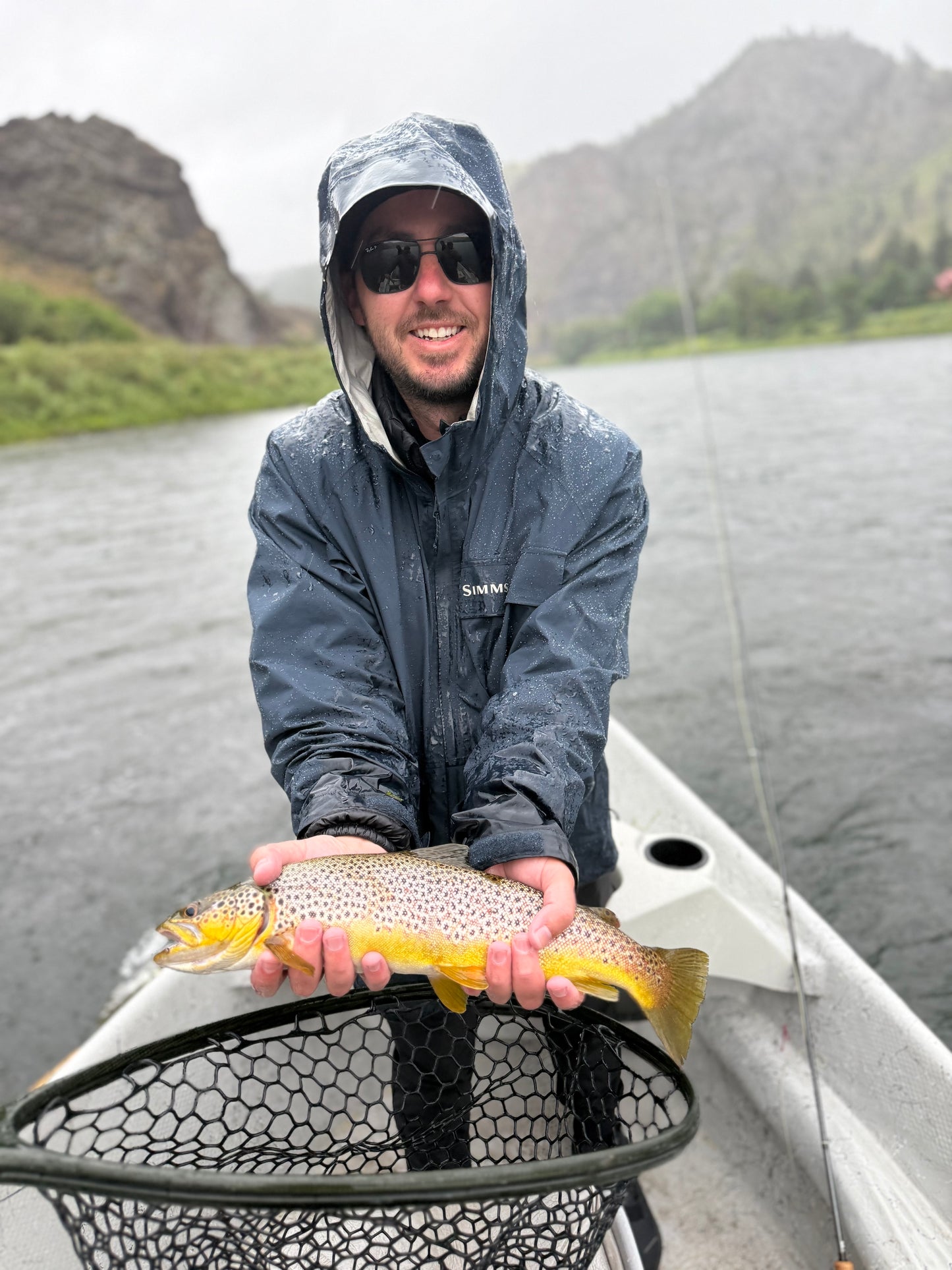 Man holding a fish on a boat with mountains in the background