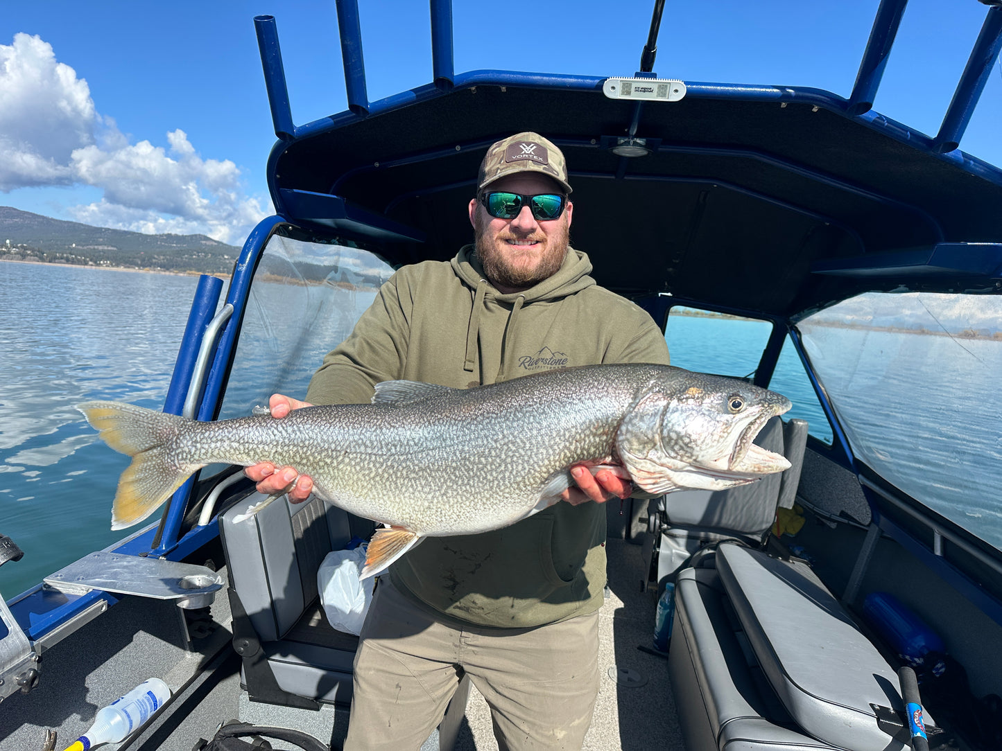 Man holding a large fish on a boat with a scenic background