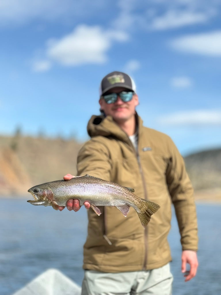 Man holding a large fish by a body of water with a blue sky.